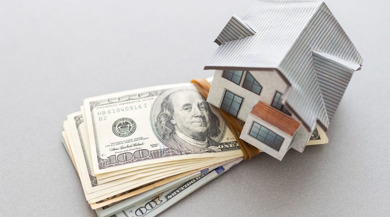 Wooden model of a house on top of a file of dollar bills to support US housing market article