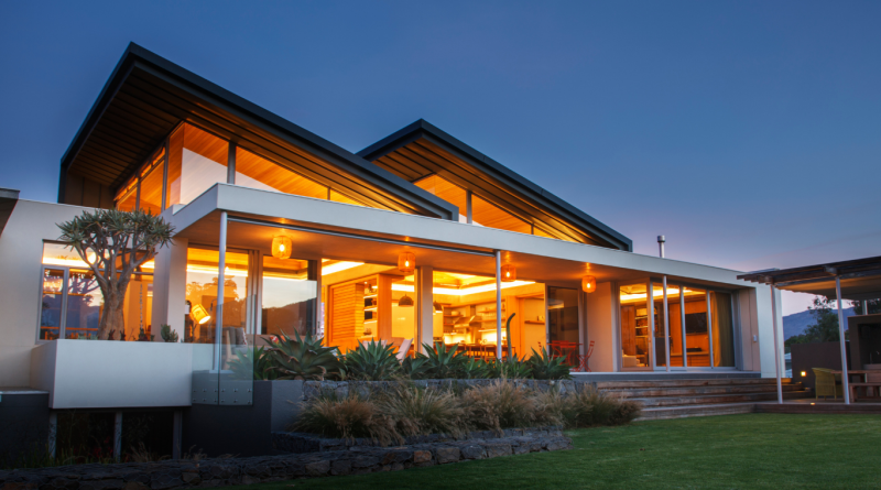 Modern luxury home with large glass windows and warm interior lighting, available as a celebrity home vacation rental.