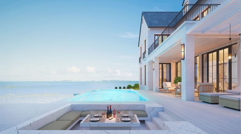 Luxury beachfront house with a marble sunken dining area beside an infinity pool, overlooking a calm ocean under a clear blue sky.
