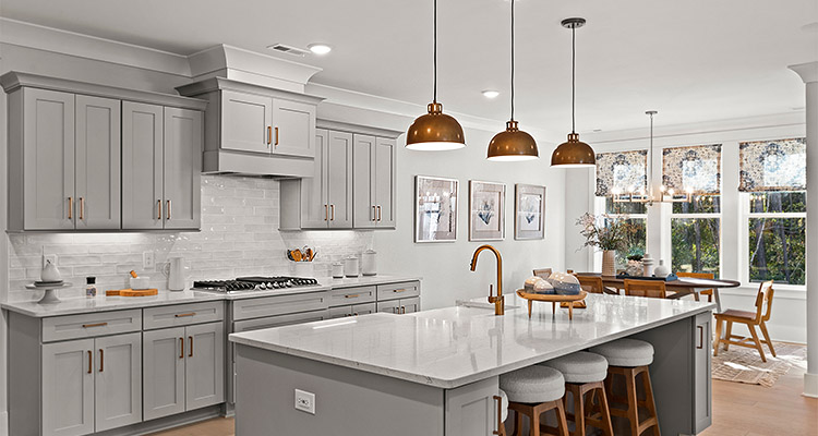 a modern, open-concept kitchen. The kitchen features light gray shaker-style cabinets with brass hardware, white countertops, and a white subway tile backsplash