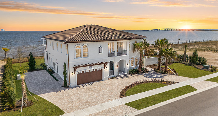 a luxury Mediterranean-style waterfront property with a multi-level design with a tiled roof, white exterior walls, and a paved circular driveway