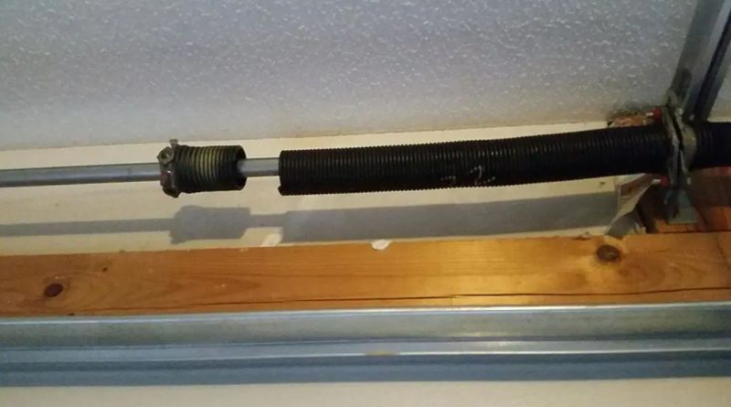 Broken torsion spring on a residential garage door, showing a visible gap in the coil mounted above the door track.